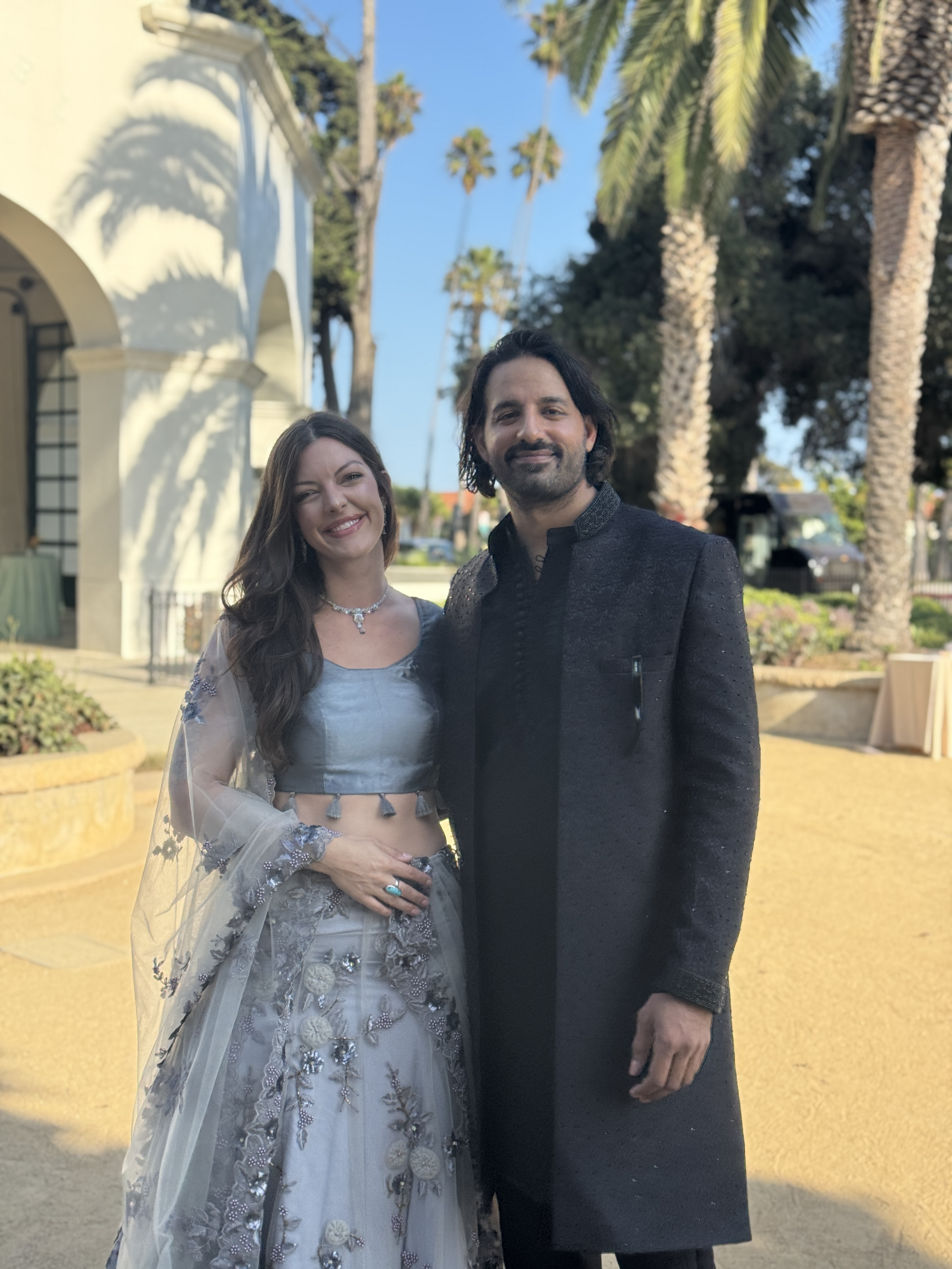 The founders of Reunited dressed in South Asian attire in front of a sunny palm-lined courtyard